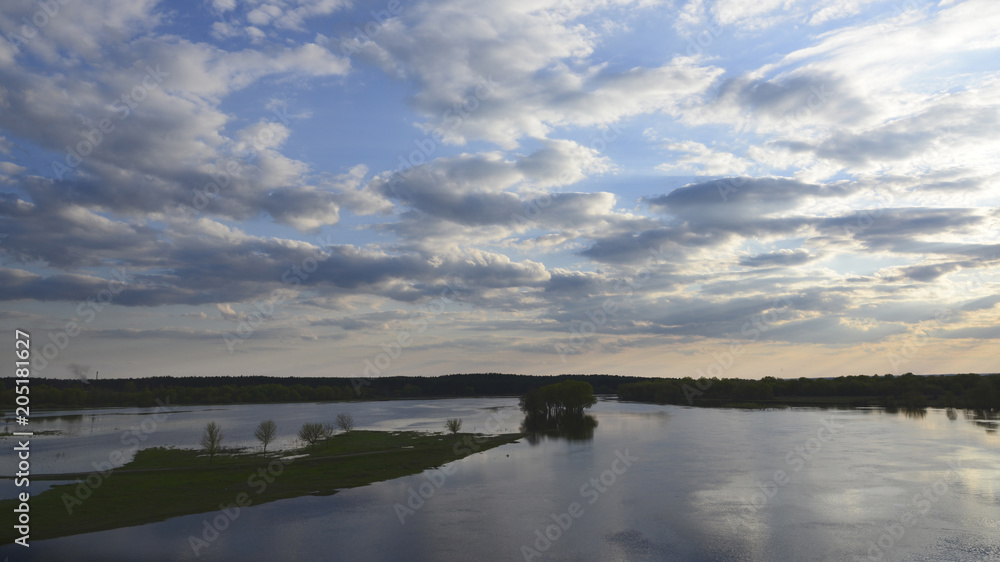 Photo of the spilling on the river in spring, green meadow and bright sky with small clouds