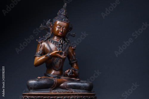 Vajrasattva's sculpture sitting with a dorje in one hand and a hand bell in another, on black background. Vajrasattva - a secret form of Buddha Samantabhadra.