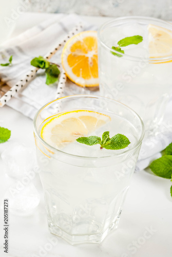 Summer refreshing drinks, mojito or lemonade with fresh mint, slices of lemon, ice, on a light background. copy space