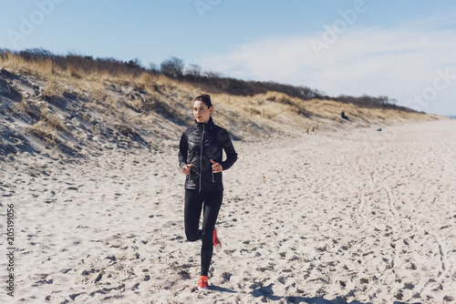 Fit athletic woman jogging along a sandy beach