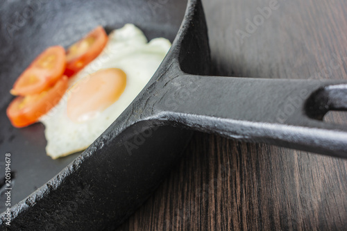 fried egg with tomatoes in a cast-iron frying pan on a wooden table photo