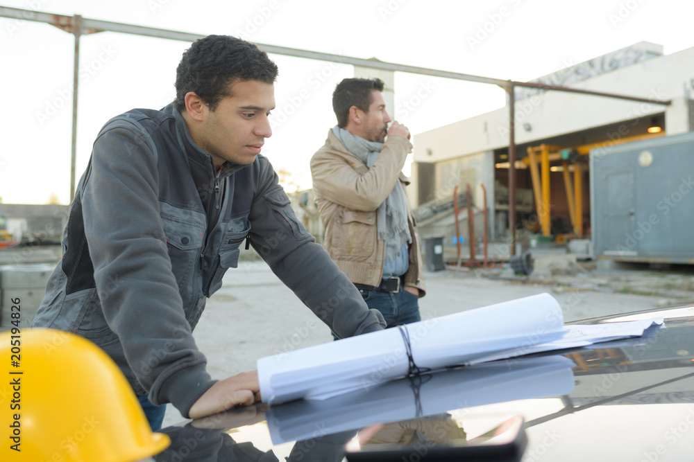 male architect examining blueprint outside industry