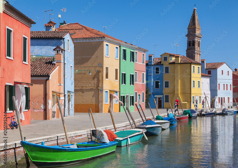 Colorfull facade Houses and bell tower on the island of Burano plus reflection in the water. Waterways with traditional boats