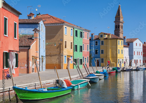 Colorfull facade Houses and bell tower on the island of Burano plus reflection in the water. Waterways with traditional boats