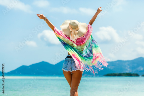 Beautiful girl is standing on the beach by the sea, wearing a pareo straw hat sunglasses, hands in the side gesture of freedom, summer vacation travel, a sense of joy photo