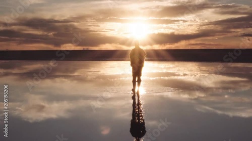 Silhouette of man walking on an incredible panorama of Uyuni salt flats at the golden sunset. Bolivia.	