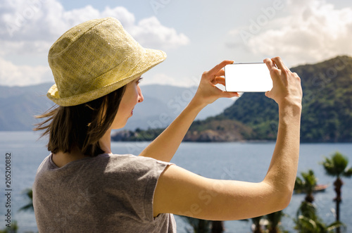 Portrait of a smiling woman casual yellow hat summer holiday holding smartphone on sea beach palm mountain sunny day background