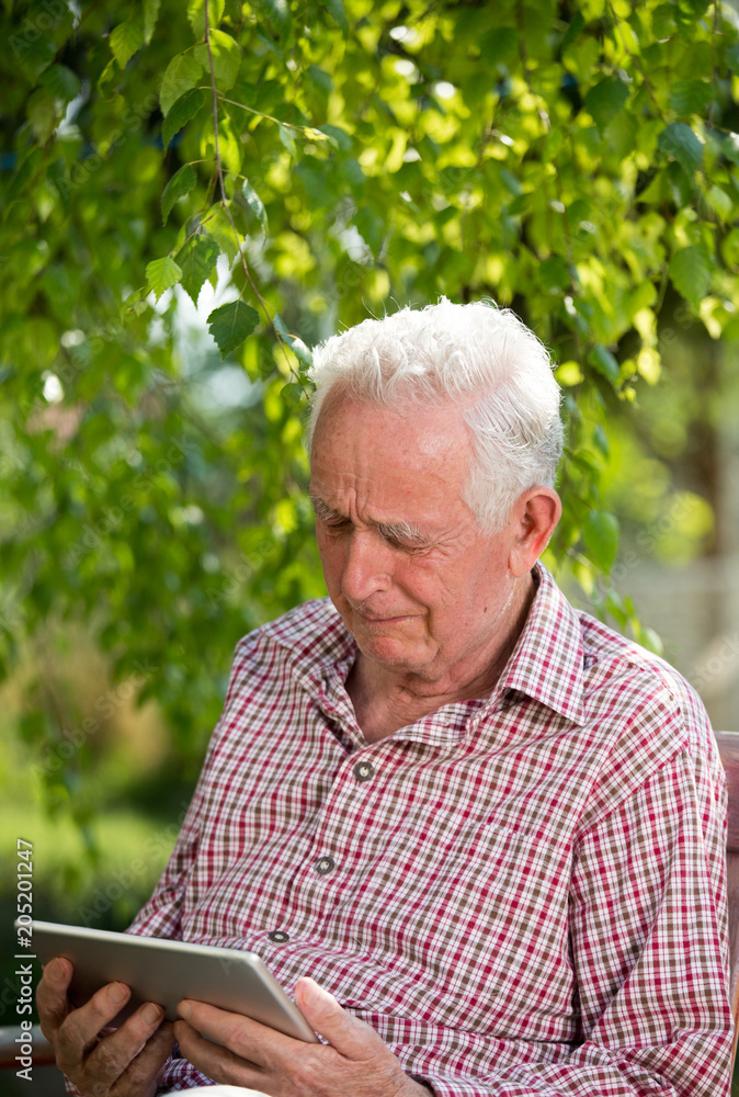 Old man with tablet crying in garden Old man with tablet crying in garden