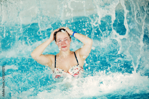 A girl in an aquapark in a pool with blue water laughs and smiles