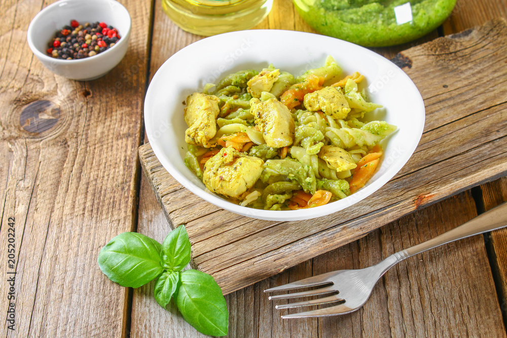 Pasta with chicken pieces and pesto sauce on an old wooden table. Pasta with chicken pieces and pesto sauce on an old wooden table.