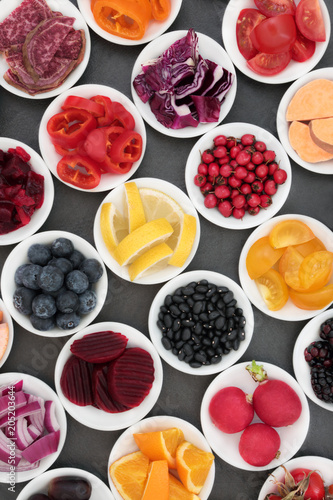 Health food with fruit, vegetables and pulses in porcelain bowls on slate background, foods very high in antioxidants, anthocyanins, fibre, vitamins and minerals.