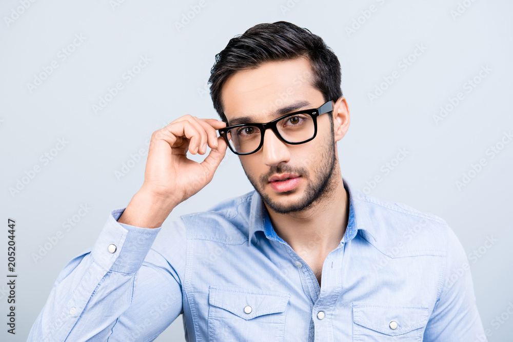 Head shot portrait of tempting seductive man with black hair in glasses holding eyelet of spectacles on his face virile sight looking at camera isolated on grey background Head shot portrait of tempting seductive man with black hair in glasses holding eyelet of spectacles on his face virile sight looking at camera isolated on grey background