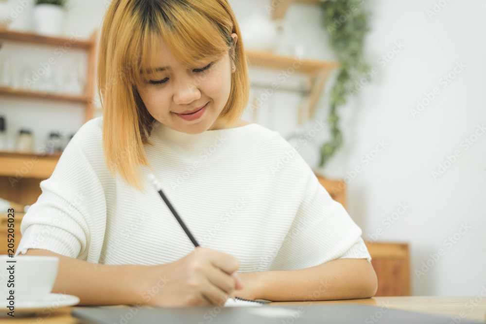 Beautiful young smiling asian woman working on laptop while sitting in a living room at home. Asian business woman working in her home office. Enjoying time at home.