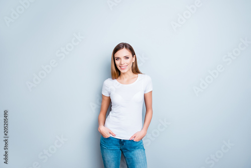 Portrait of cheerful cute girl in white t-shirt holding her hands in pocket of pants isolated on grey background looking at camera