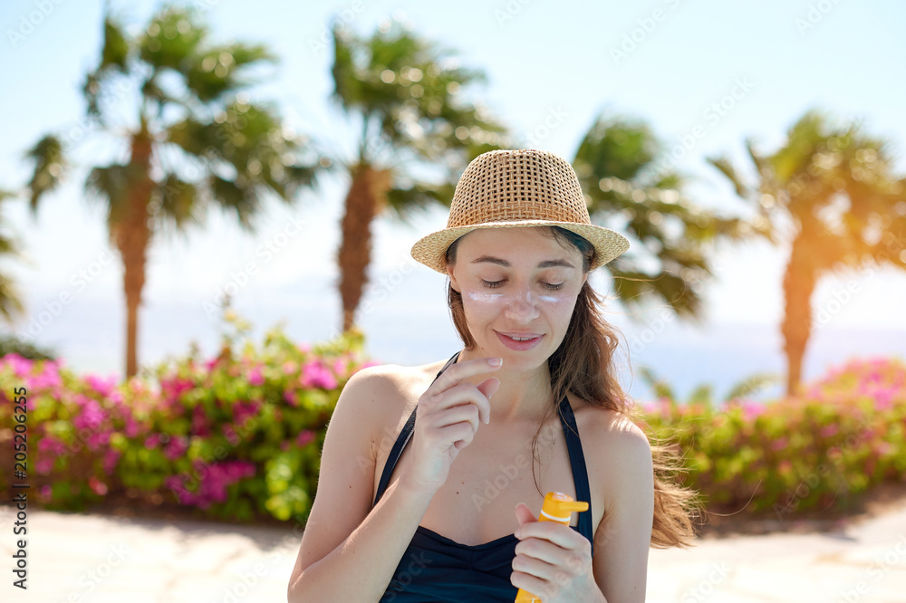 Portrait of a beautiful young woman, smiling in a swimsuit smeared face with sun protection cream in hat on sea background. Concept: sea sun and travel vacation freedom, enjoy sunburn heat hot