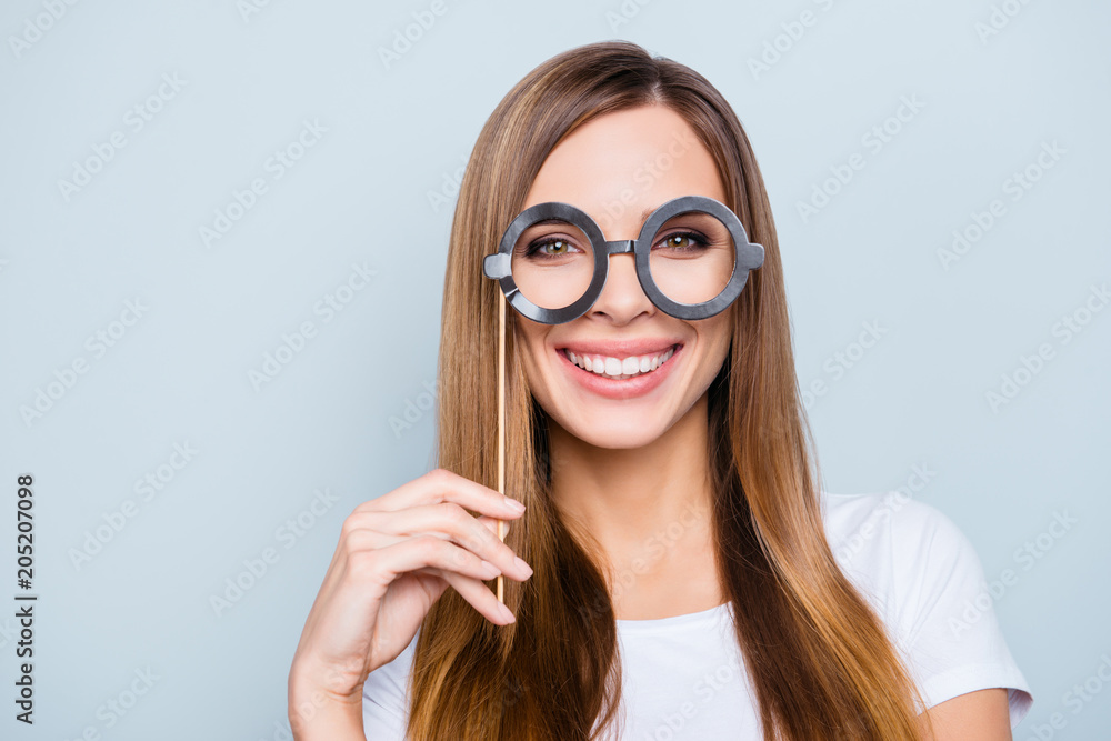 Close up portrait of playful positive girl holding black carton glasses on stick looking at camera isolated on grey background