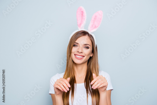 Portrait of childish playful girl wearing bunny ears holding hands like hare looking at camera isolated on grey background