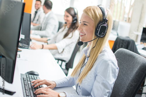 Foto Beautiful blonde woman telephone operator talking with customer in call center