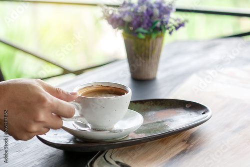 Closeup hand of male holding a coffee cup on wooden table in morning time. Feel refreshed and relaxing with the coffee drinking concept. 