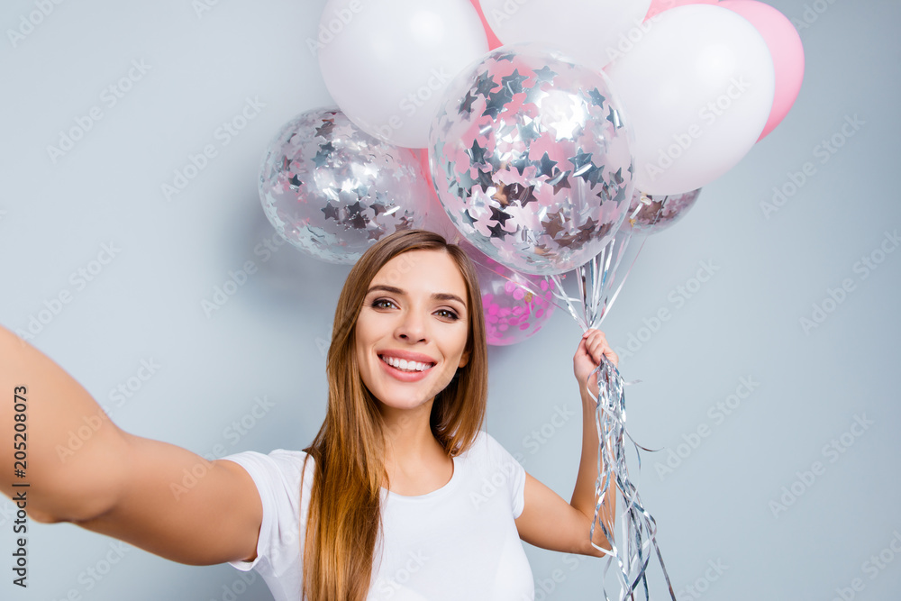 Self portrait of creative positive girl in casual outfit having pink and white air balloons in hand shooting selfie on front camera isolated on grey background Self portrait of creative positive girl in casual outfit having pink and white air balloons in hand shooting selfie on front camera isolated on grey background