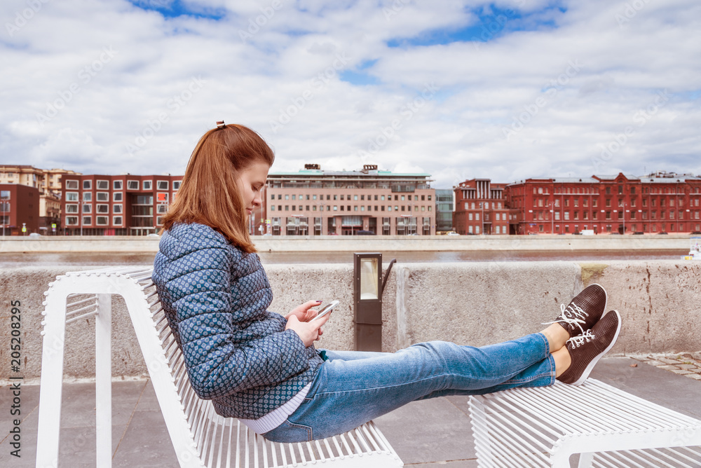 Attractive girl sitting relaxed on the waterfront and reads the news on your phone