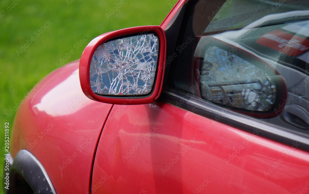 Car with broken side door mirror. Red car in green background. Asociative.