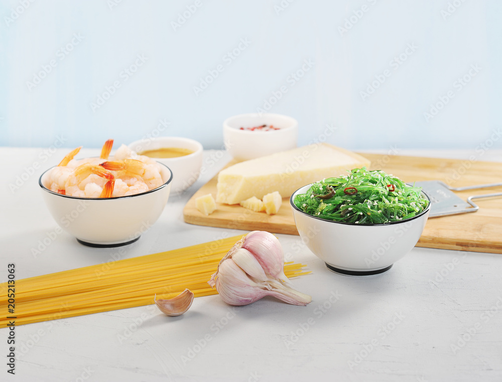A set for cooking pasta with shrimps and seaweed. Spaghetti, chicken salad, shrimp, spices, garlic, nut sauce, parmesan cheese and grater for cheese. Light background. Close-up. A set for cooking pasta with shrimps and seaweed. Spaghetti, chicken salad, shrimp, spices, garlic, nut sauce, parmesan cheese and grater for cheese. Light background. Close-up.