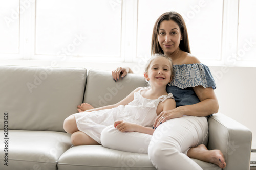 Portrait of beautiful mother and her little daughter sitting together on couch