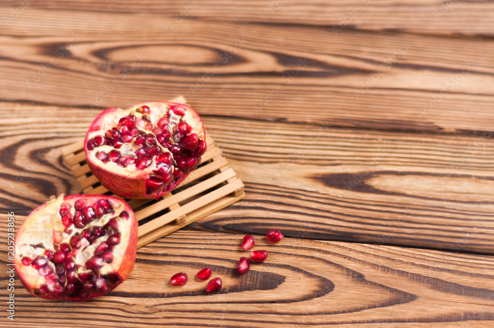 One half of red fresh ripe pomegranate with seeds on pallet beside one piece of pomegranate and scattered seeds on old brown weathered wooden planks One half of red fresh ripe pomegranate with seeds on pallet beside one piece of pomegranate and scattered seeds on old brown weathered wooden planks