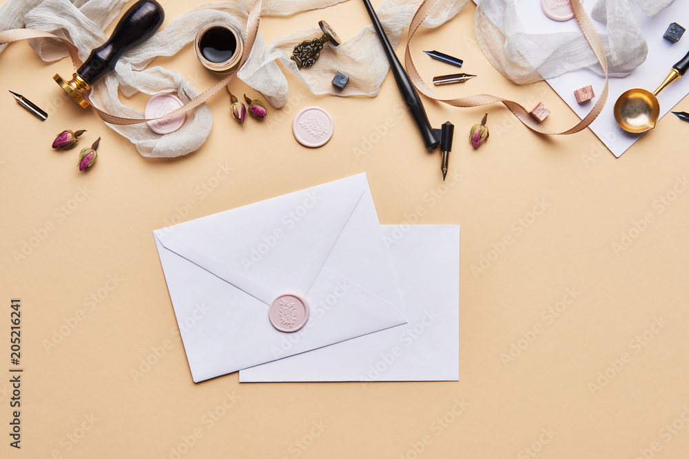 Fototapeta premium Flat lay of feminine desk workspace with copy space. Calligraphic style, paper and envelope on beige background. Top view of home office.