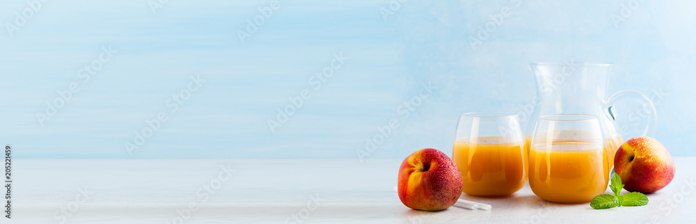 peach juice in glasses and a decanter and fresh peaches with leaves on a table. blue background. copy space peach juice in glasses and a decanter and fresh peaches with leaves on a table. blue background. copy space