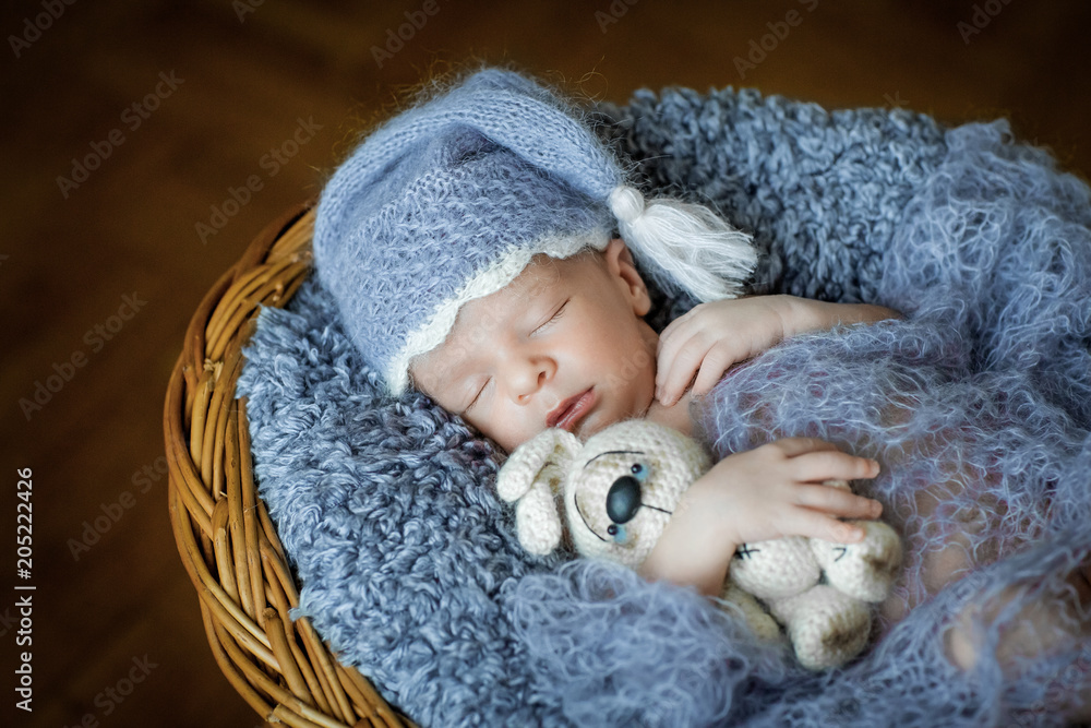 Newborn boy in hat is sleeping in the basket with toy Newborn boy in hat is sleeping in the basket with toy
