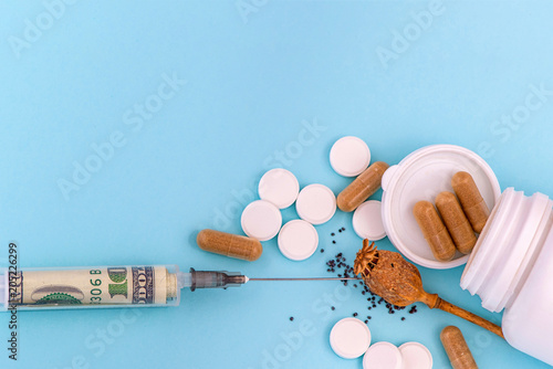 Drug opium poppy, pills and syringe with a dollar inside. On blue background. photo