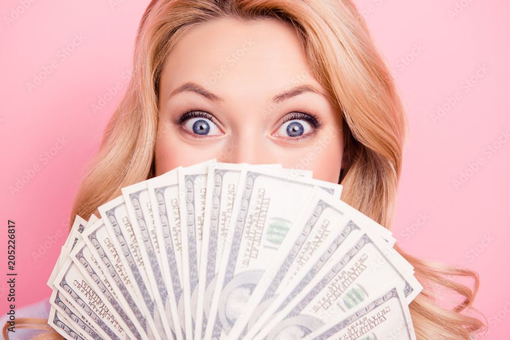 Close up portrait of shocked surprised girl peeking out fan of much money with wide open eyes hiding her half face isolated on pink background Close up portrait of shocked surprised girl peeking out fan of much money with wide open eyes hiding her half face isolated on pink background