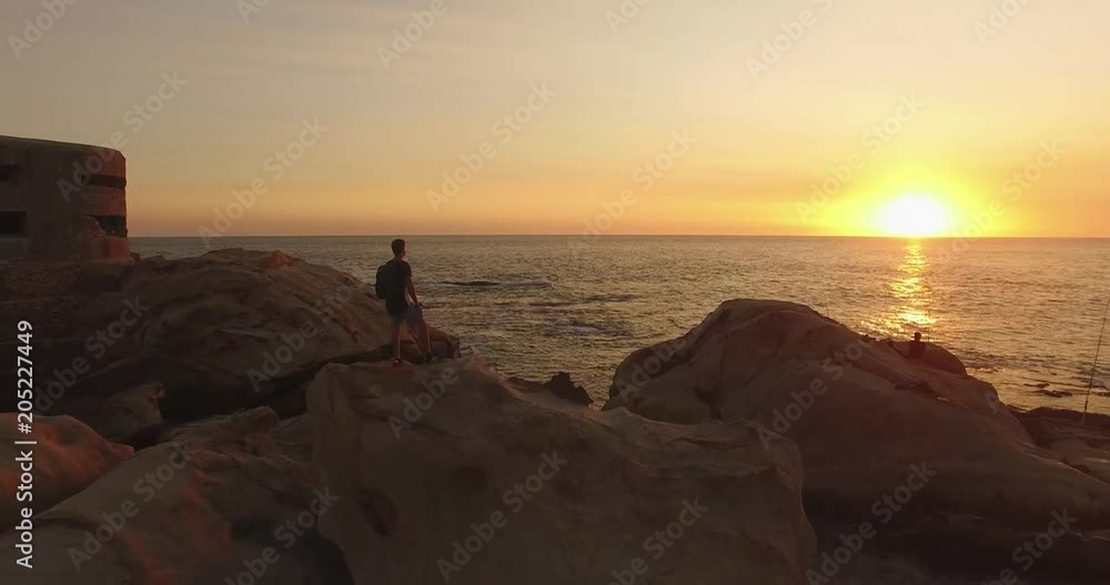 Aerial view, flyover of one man on top of rock with the arms raised at sunset in the beach Aerial view, flyover of one man on top of rock with the arms raised at sunset in the beach