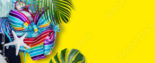 Quadro su tela Colorful bikini and clothes in luggage with tropical leaves on yellow background