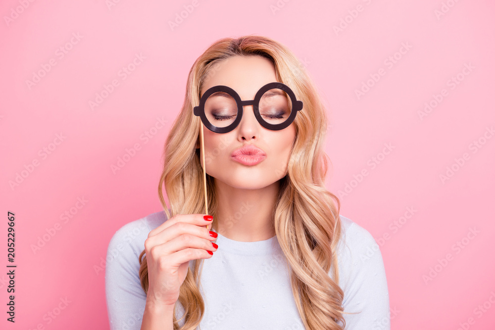 Portrait of cute lovely flirting girl having black carton glasses on stick blowing sending kiss with pout lips and close eyes isolated on pink background
