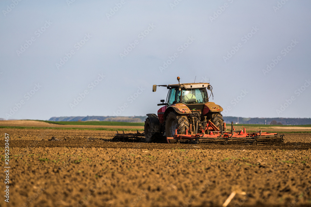 Fototapeta premium Farmer in tractor preparing land with seedbed cultivator as part of pre seeding activities in early spring season of agricultural works at farmlands.
