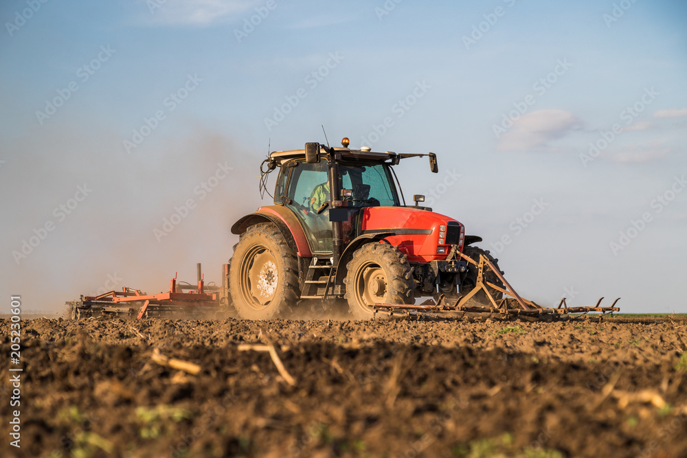 Fototapeta premium Farmer in tractor preparing land with seedbed cultivator as part of pre seeding activities in early spring season of agricultural works at farmlands.