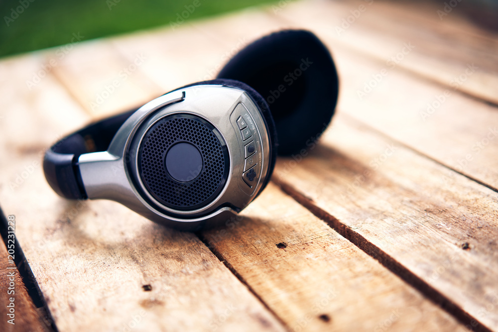 A 45 degree view of a set of wireless headphones lying on a rustic wooden table outside. Styling and grain effect added to image. A 45 degree view of a set of wireless headphones lying on a rustic wooden table outside. Styling and grain effect added to image.