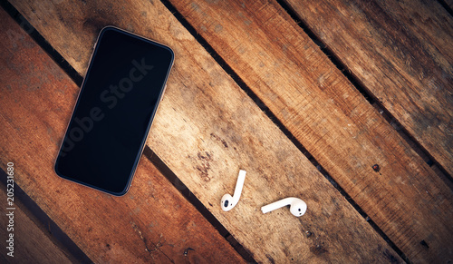 Obraz na płótnie A top view of a set of wireless earbud headphones and mobile phone blank template lying on a rustic wooden table. Styling and grain effect added to image. w salonie