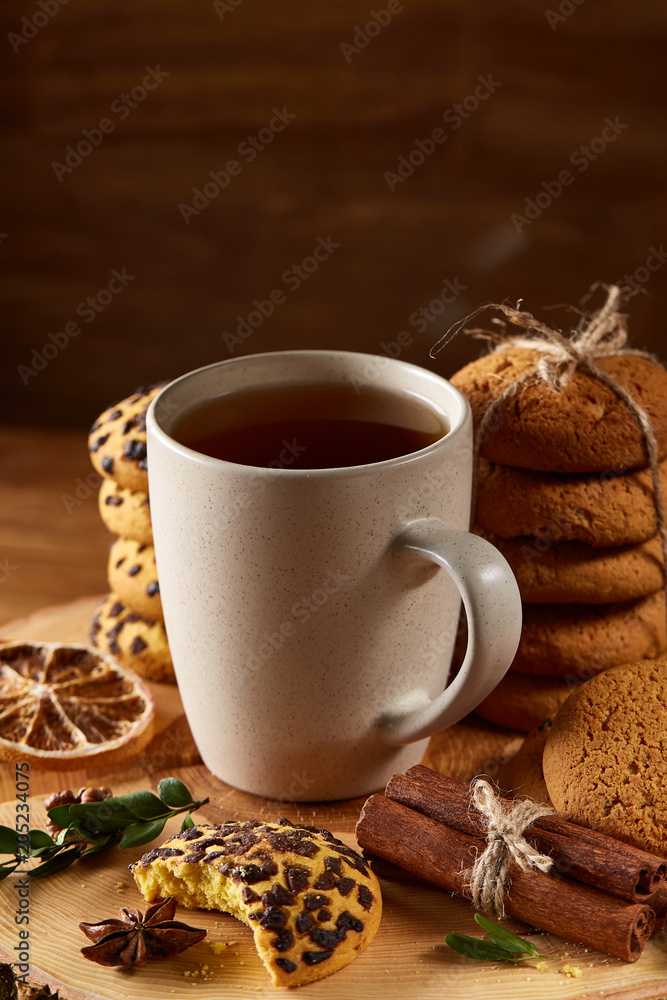 Christmas concept with a cup of hot tea, cookies and decorations on a log over wooden background, selective focus Christmas concept with a cup of hot tea, cookies and decorations on a log over wooden background, selective focus