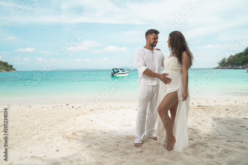 Attractive young couple on the tropical island. Beautiful woman and man wearing white clothes embracing each other and enjoying trpoical holidays vacation getaway