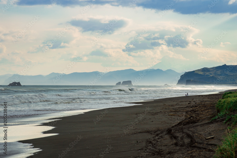Halaktyr beach. Kamchatka. Russian federation. Dark almost black color sand beach of Pacific ocean. Stone mountains and yellow grass are on a background. Light blue sky Halaktyr beach. Kamchatka. Russian federation. Dark almost black color sand beach of Pacific ocean. Stone mountains and yellow grass are on a background. Light blue sky