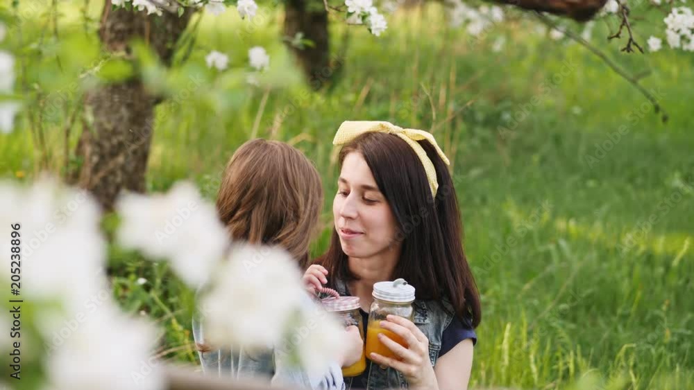 Little girl kisses the young mother on nature. In the hands of a bottle with straws and orange juice