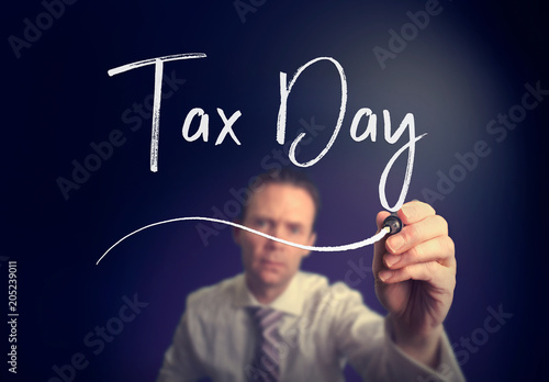 A businessman writing a Tax Day concept with a white pen on a clear screen.