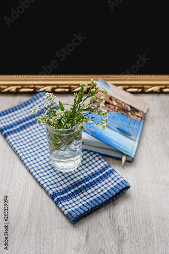 Still-life pen and diary for notes, wildflowers in a glass on a white-blue checkered napkin on a wooden background