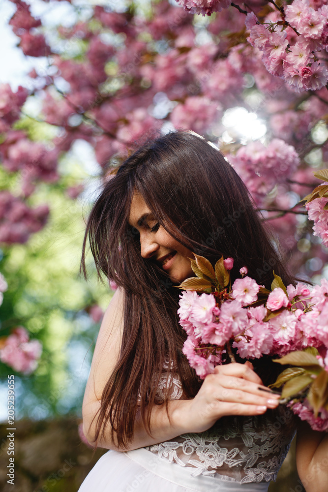 Wind blows brunette woman's hair while she poses before a blooming sakura tree