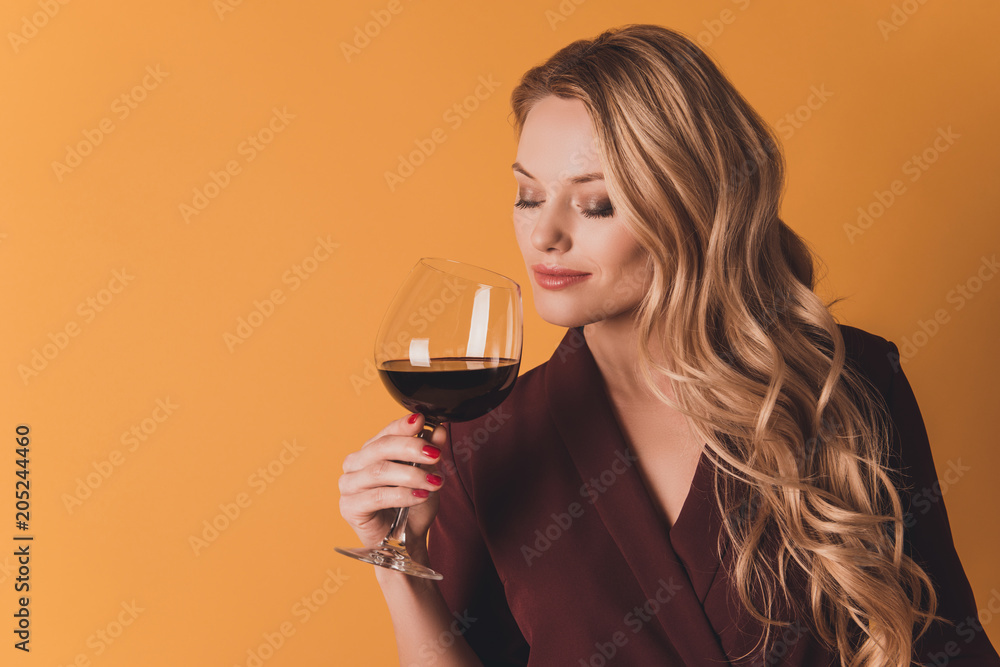 Portrait of dreamy lovely cute woman with close eyes holding glass with red wine in hand enjoying smell of beverage having fun isolated on dark yellow background Portrait of dreamy lovely cute woman with close eyes holding glass with red wine in hand enjoying smell of beverage having fun isolated on dark yellow background