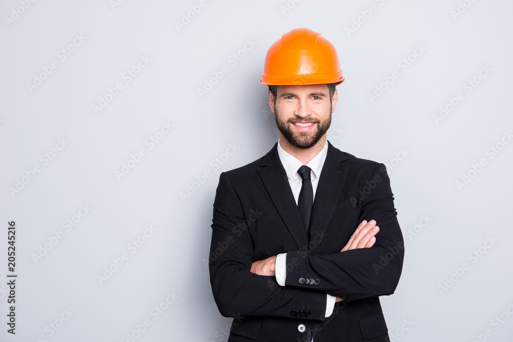 Portrait of attractive young stylish investor with stubble in orange hard hat and black tux, tuxedo with tie, looking at camera, isolated on grey background, having his arms crossed Portrait of attractive young stylish investor with stubble in orange hard hat and black tux, tuxedo with tie, looking at camera, isolated on grey background, having his arms crossed